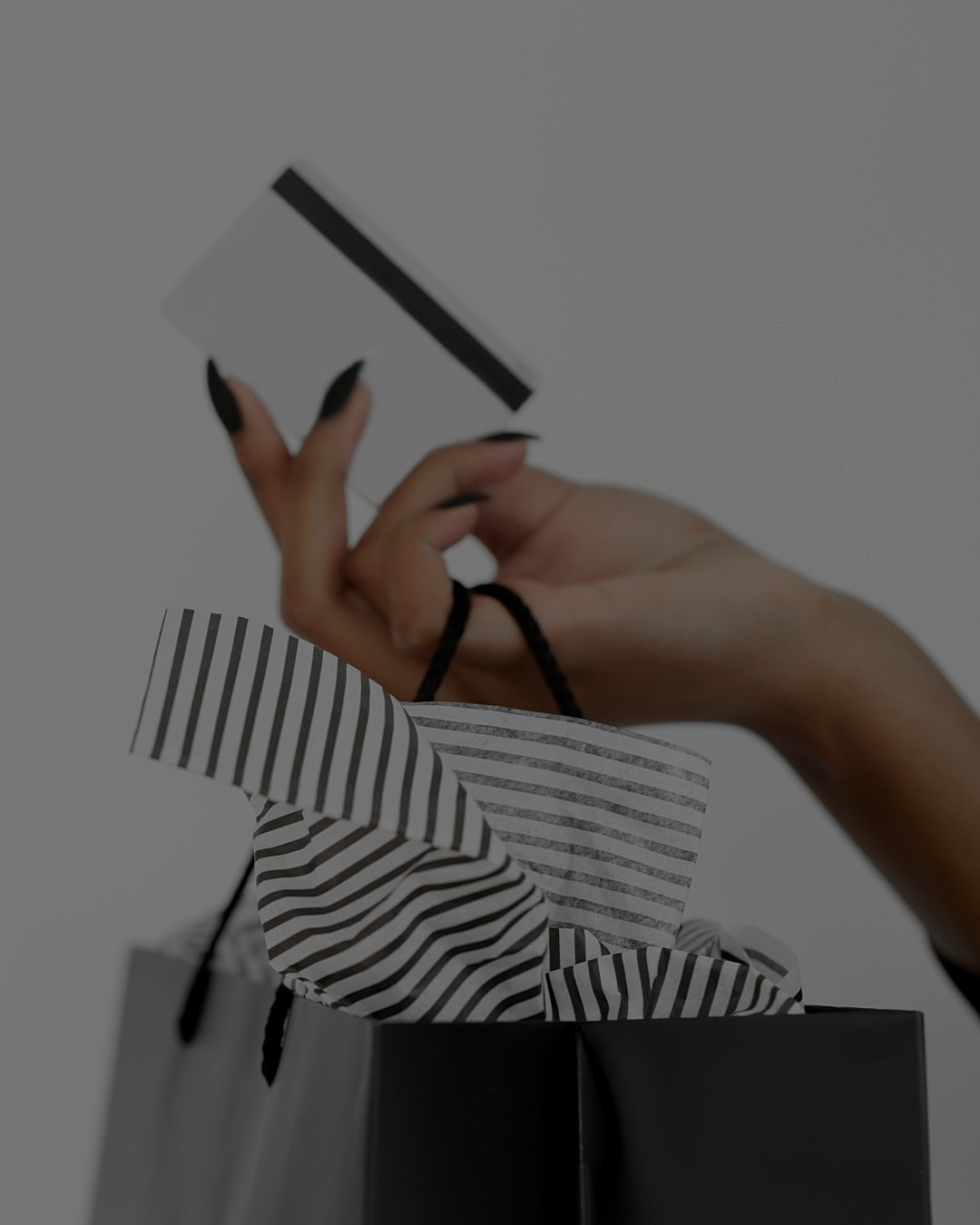 Hand holding card above black shopping bag.