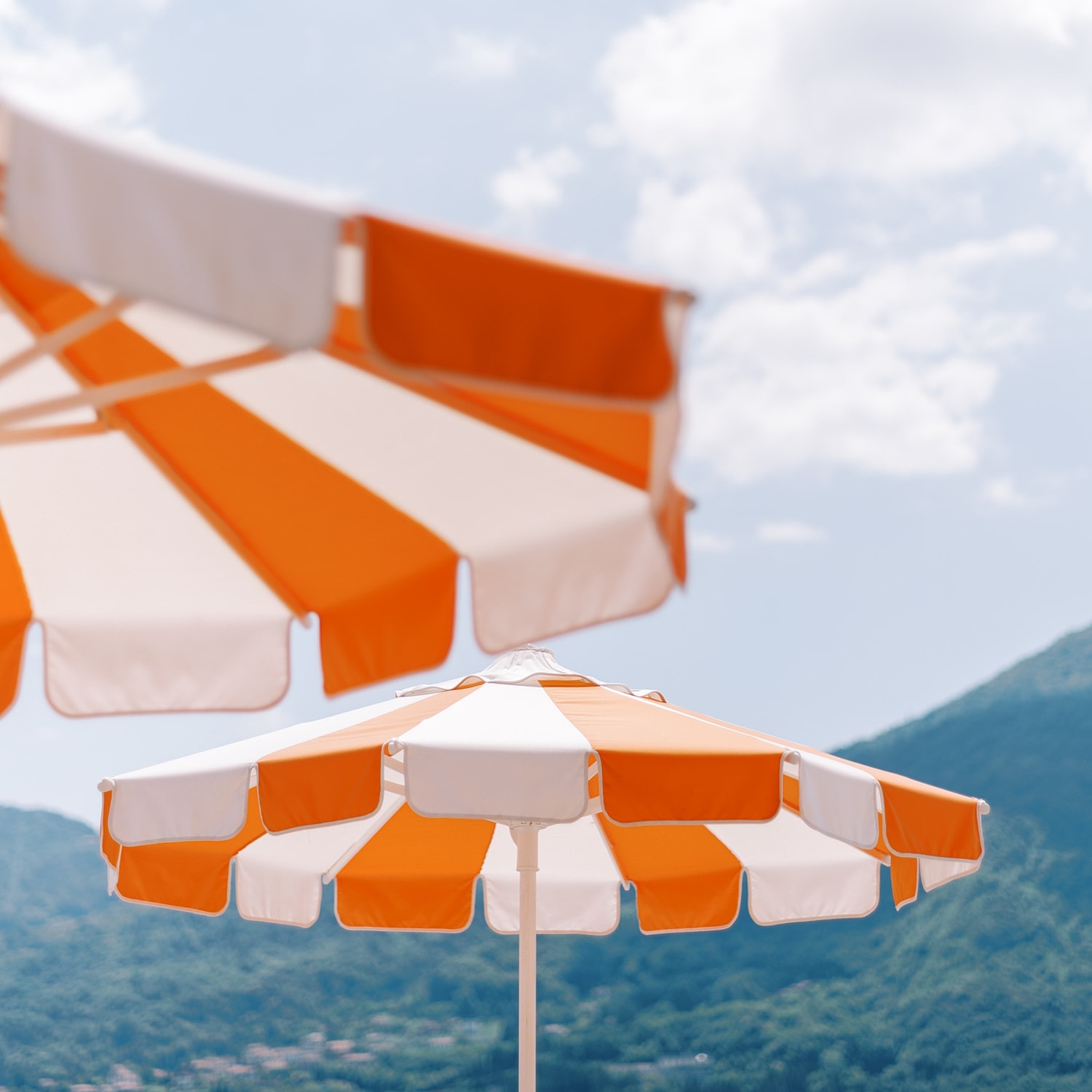 Orange and white striped beach umbrellas against mountains.
