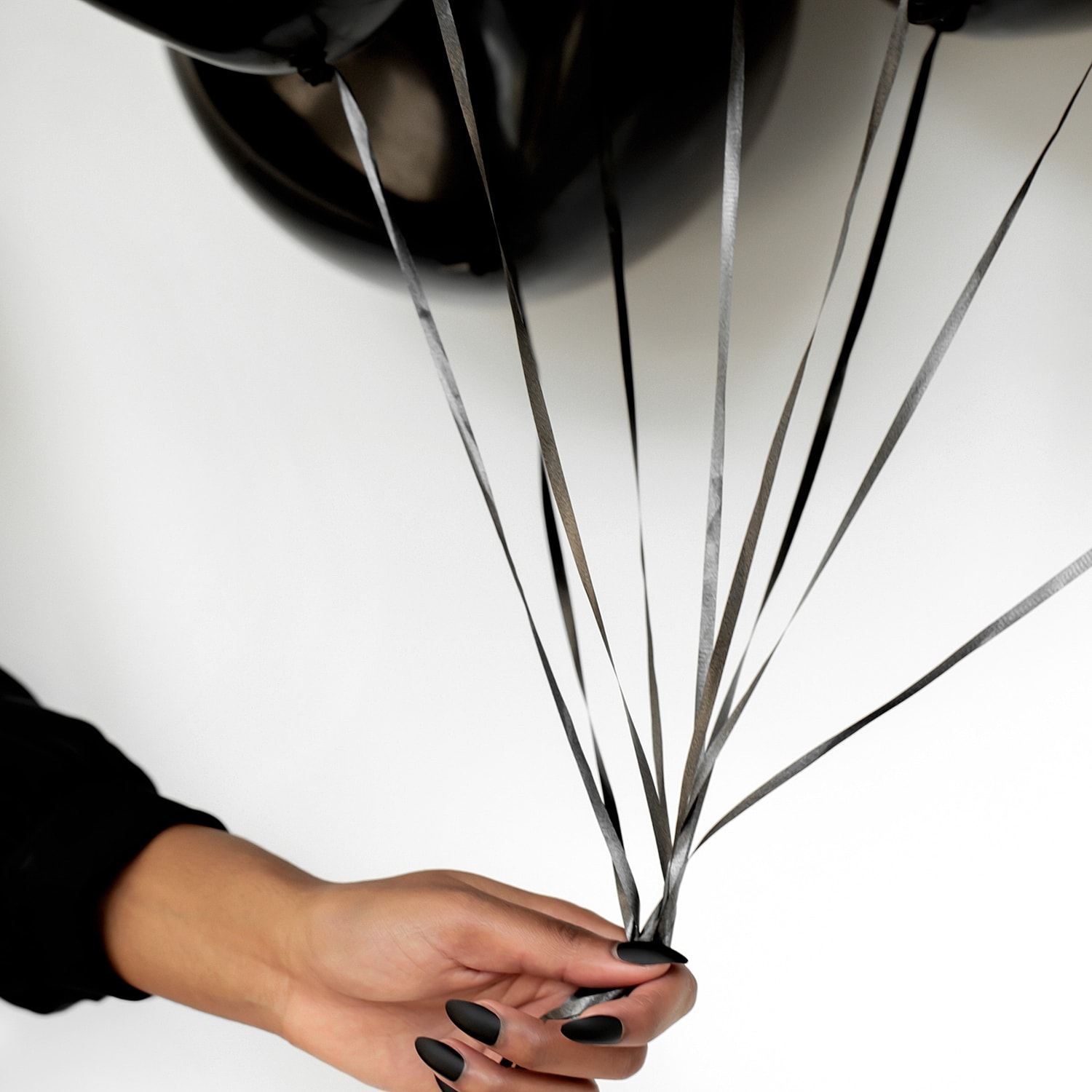 Hand holding black balloons with ribbons.