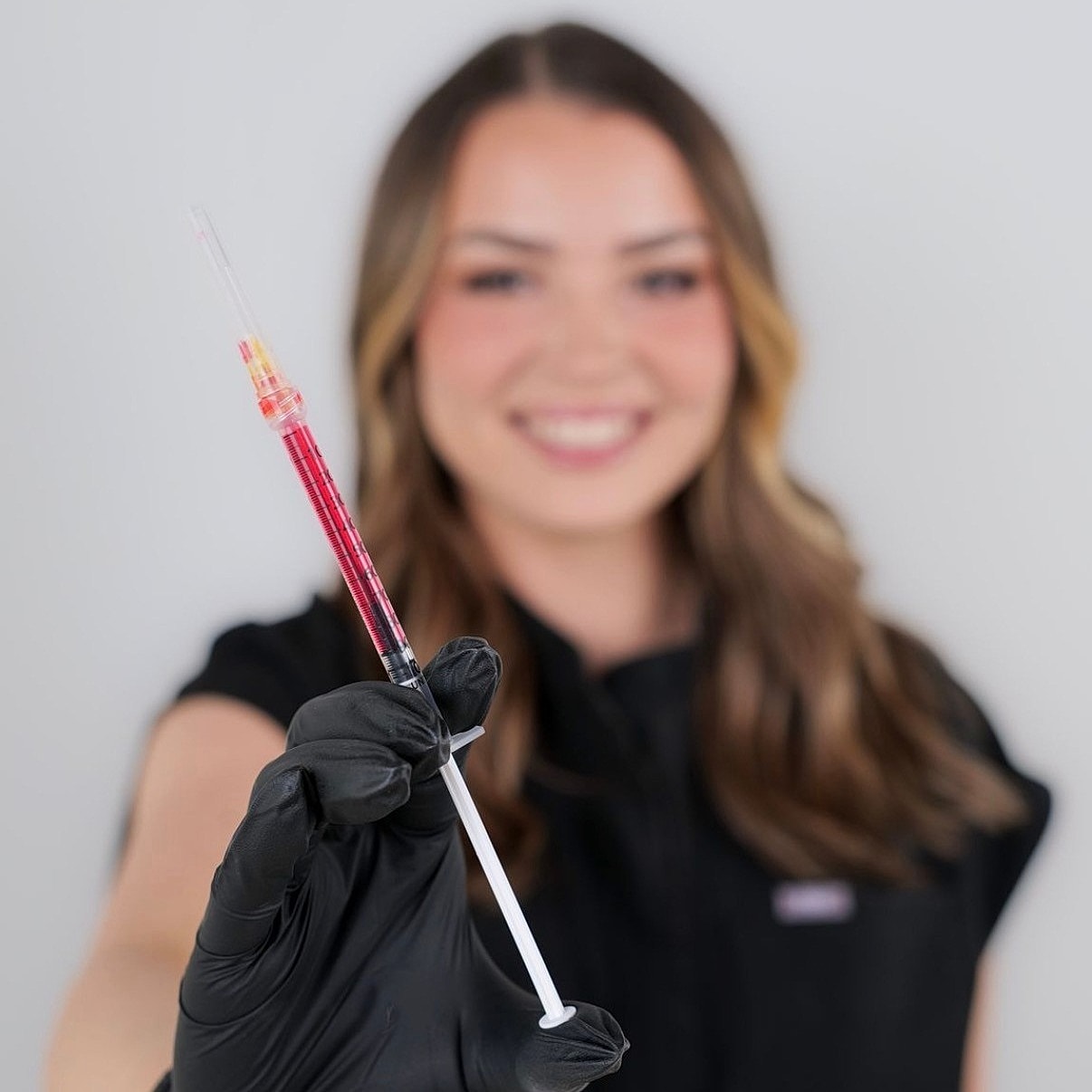 Smiling person holding a syringe with liquid.