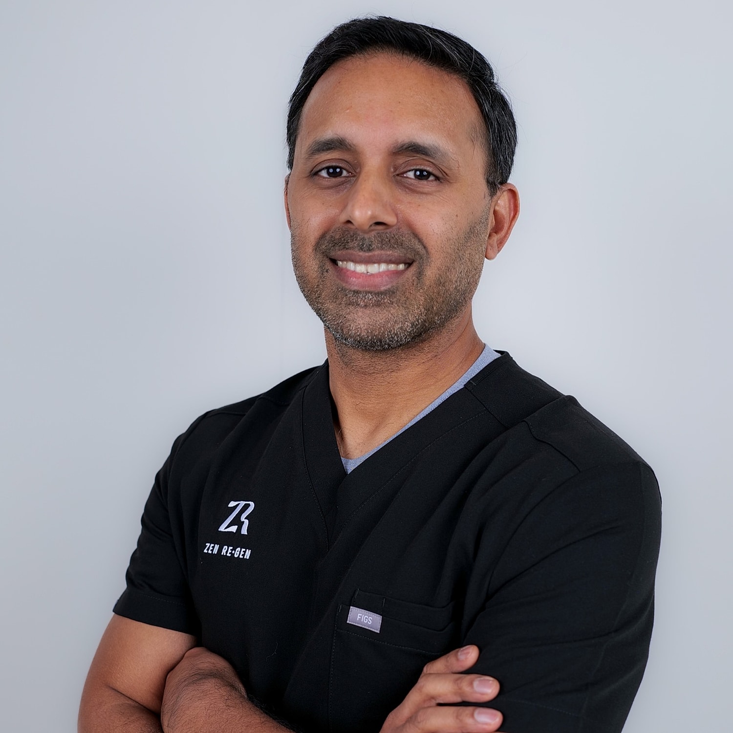 Smiling professional in medical scrubs, arms crossed.