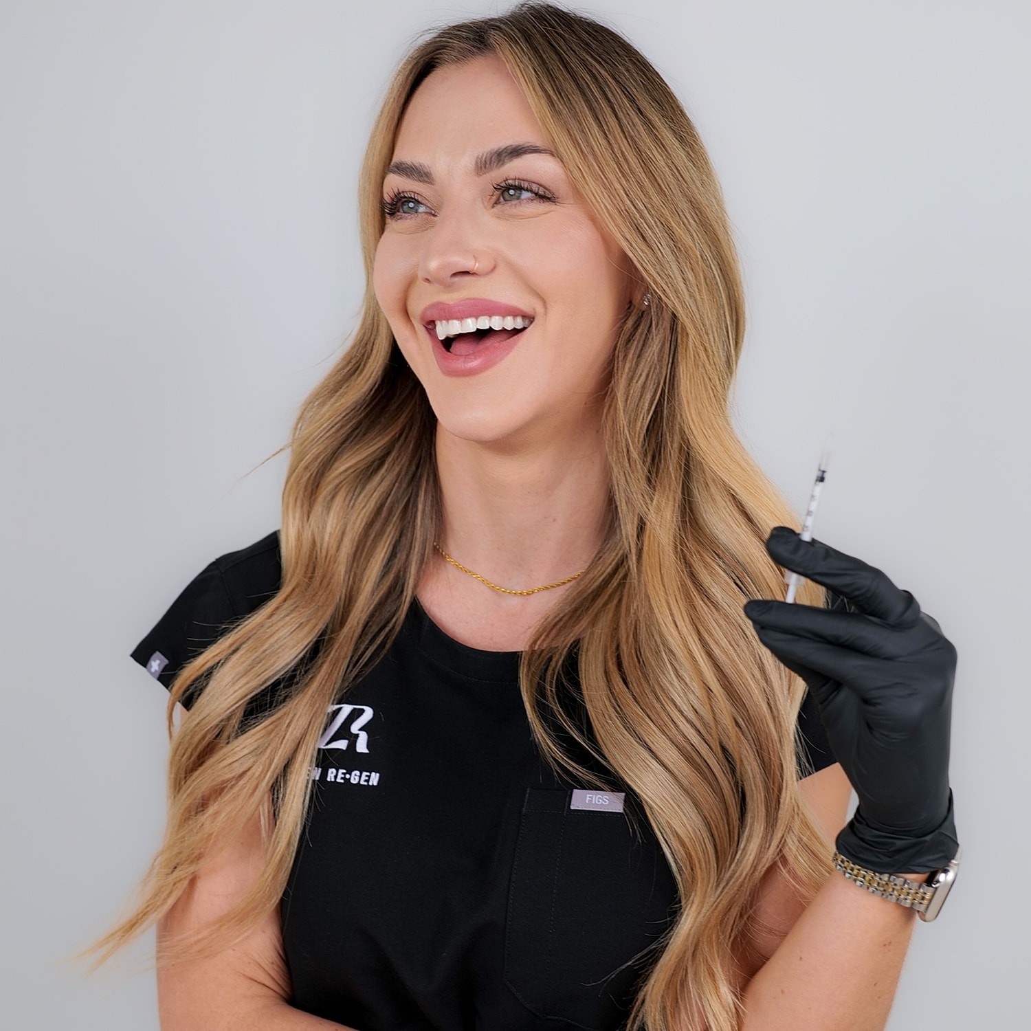 Smiling professional holding syringe, wearing gloves.