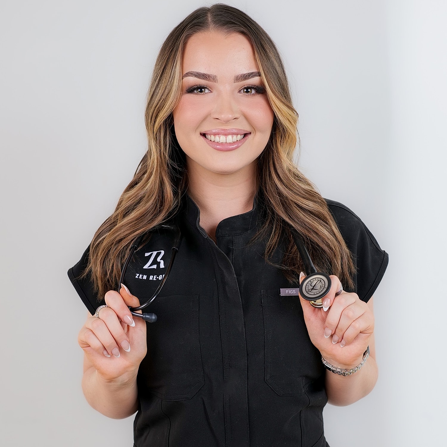 Smiling woman in medical scrubs holding a stethoscope.