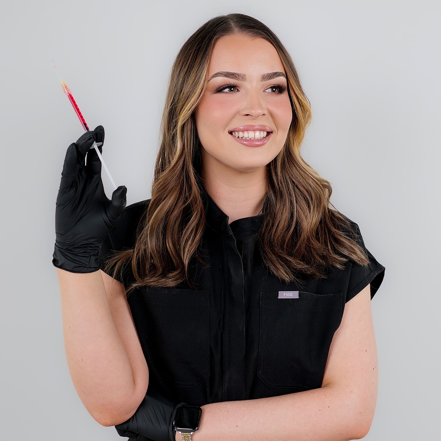 Woman smiling, holding syringe in gloved hand.
