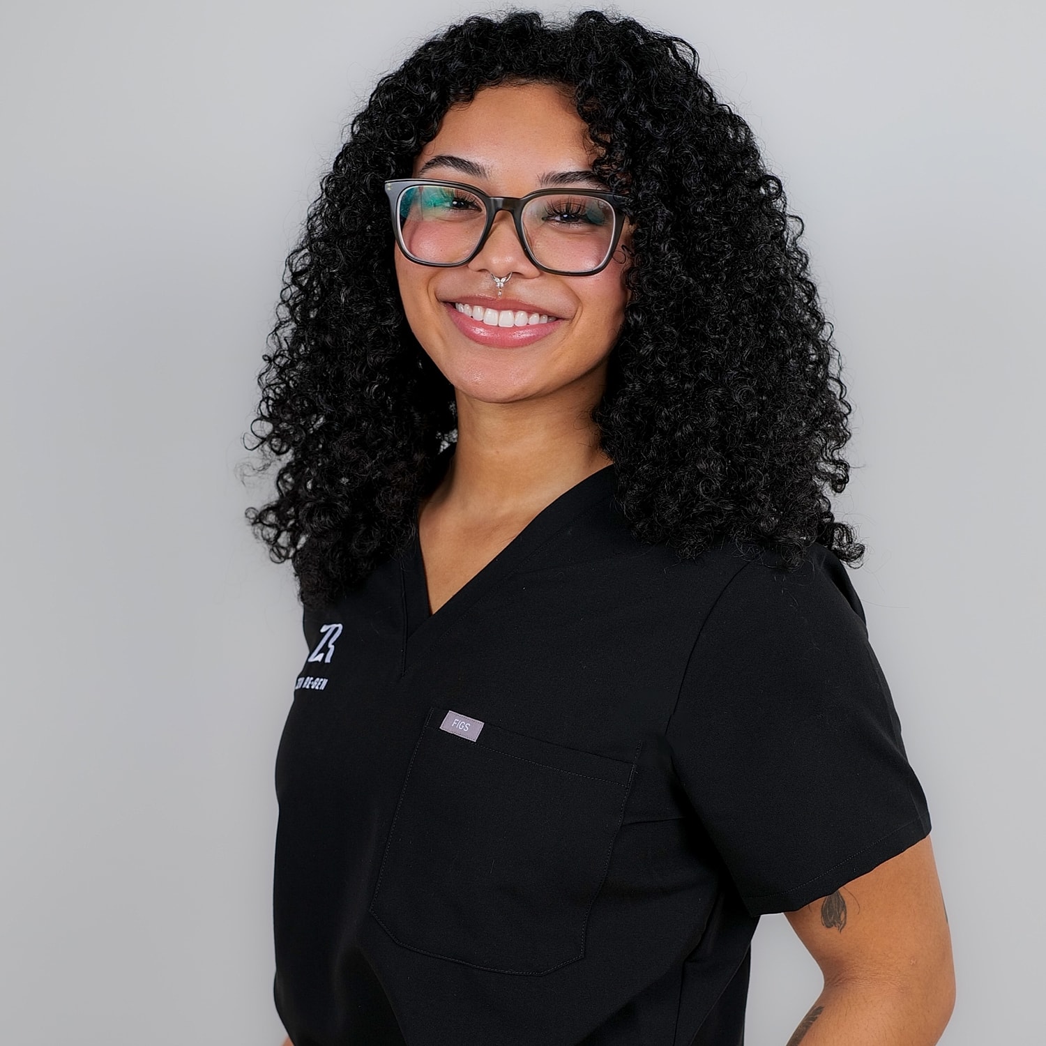 Smiling woman wearing black medical scrubs and glasses.