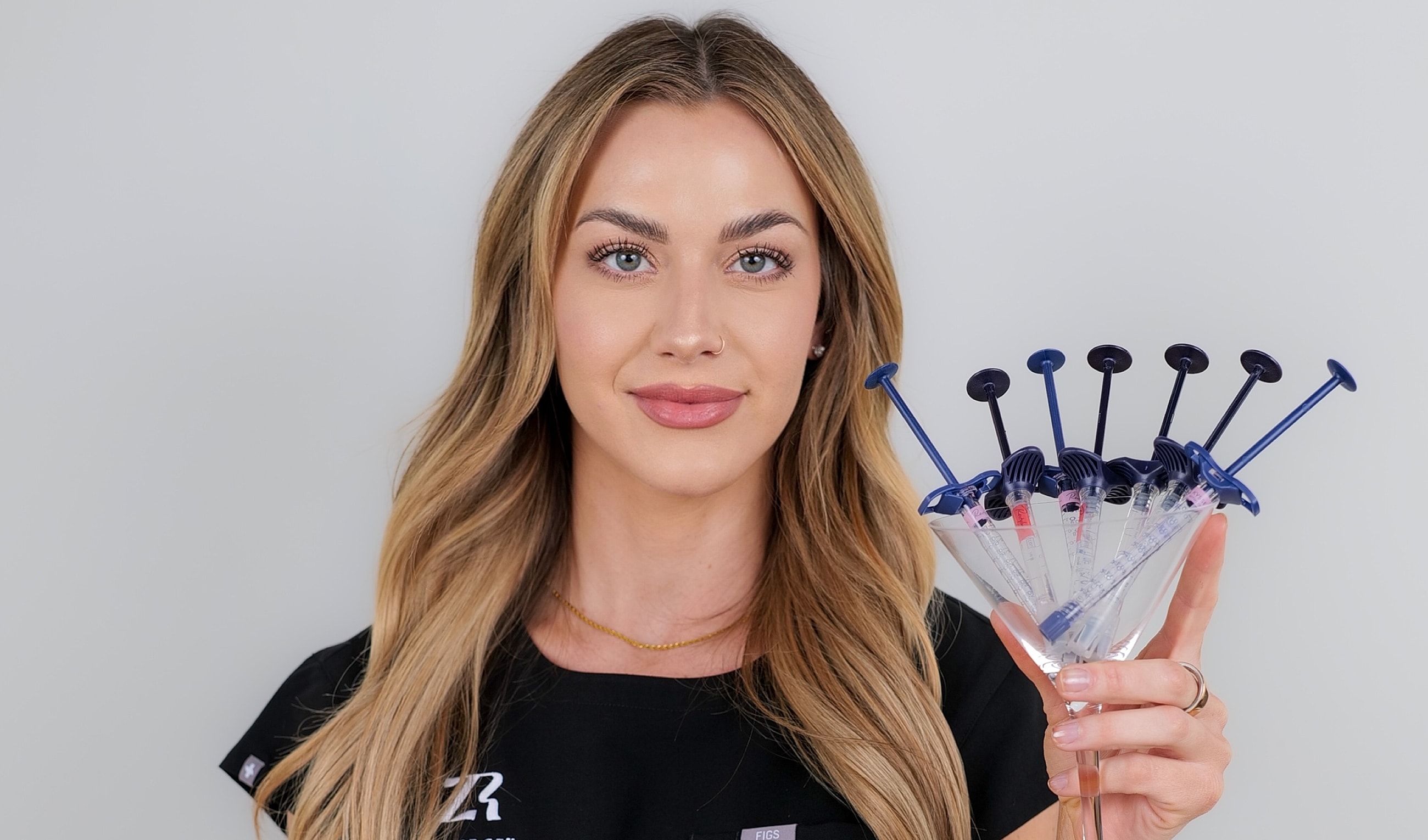 Woman holding syringes in a martini glass.